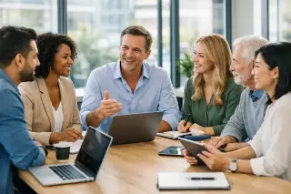 Business team of diverse professionals collaborating around a modern office table with laptops and digital devices in a bright, positive workspace.