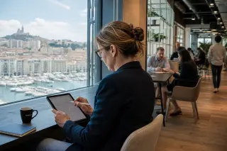 Businesswoman in a coworking lounge, deeply focused on her tablet, Marseille city view in background, with diverse professionals moving quietly around her.