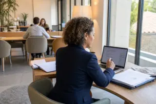 Businesswoman working thoughtfully by a window in a coworking space, natural daylight, authentic professional setting