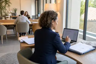 Businesswoman working thoughtfully by a window in a coworking space, natural daylight, authentic professional setting