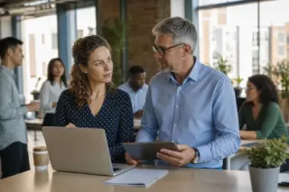 Two professionals quietly conferring by a high table in a modern coworking space, natural daylight and a bustling yet understated office atmosphere.