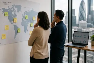 Two professionals in a modern office quietly studying a world map with notes by a window, suggesting thoughtful international business planning.