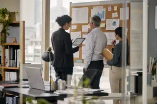 Executives in a modern office intently reviewing trend charts and notes by a window, soft daylight illuminating their thoughtful, natural interaction.