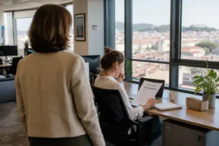 HR manager observing a thoughtful employee reviewing training materials by a window in a softly lit, modern open office