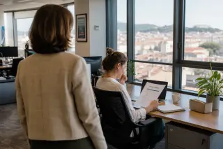 HR manager observing a thoughtful employee reviewing training materials by a window in a softly lit, modern open office