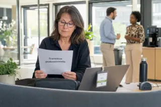 Mid-career professional reading a transition document at her desk in a sunlit open-plan office, with colleagues quietly chatting in the background.