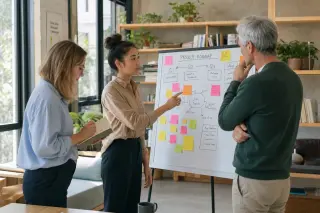 Three diverse professionals collaborating at a whiteboard in a bright coworking space, absorbed in discussion and notes, with natural light highlighting a candid team moment.