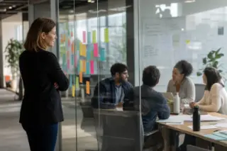 Un manager observe ses collègues à travers une cloison vitrée couverte de post-it, en pleine discussion.