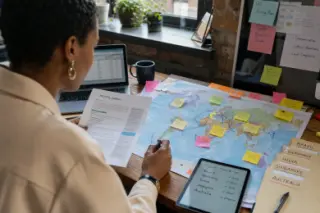 Des mains annotent une carte du monde avec des post-it, à côté de documents RH et d'une tablette.