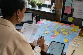 Des mains annotent une carte du monde avec des post-it, à côté de documents RH et d'une tablette.